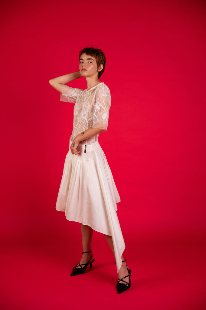 "Model wearing Amelia Lace Pleated Dress in white, side view, showing intricate lace detail and flowing pleats"
